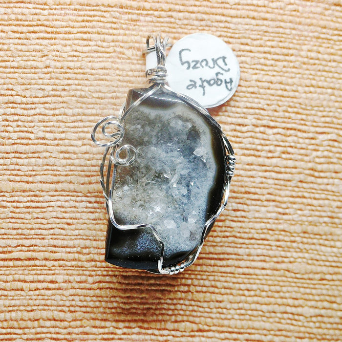 Crystal pendant with silver wire wrapping on a textured beige surface