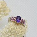Silver ring with a purple gemstone and smaller pink stones on a textured white background