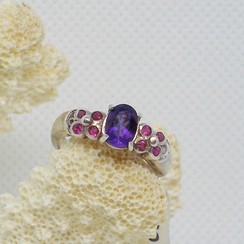 Silver ring with a purple gemstone and smaller pink stones on a textured white background