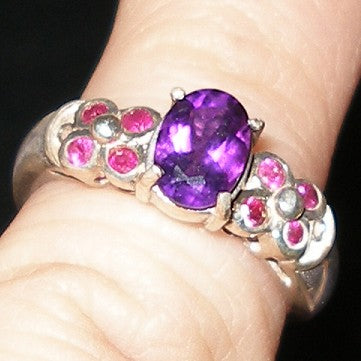 Ring with purple gemstone and pink stones on a finger against a dark background