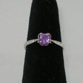 Silver ring with a purple gemstone on a black stand against a gray background