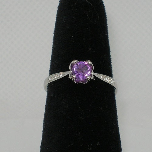 Silver ring with a purple gemstone on a black stand against a gray background