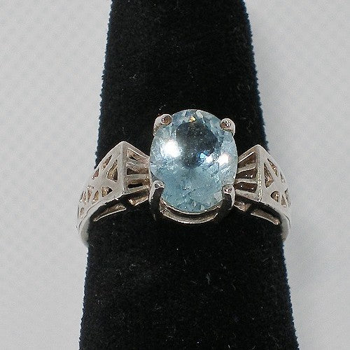 Silver ring with a blue gemstone on a black stand against a gray background
