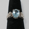 Silver ring with a blue gemstone on a black stand against a gray background