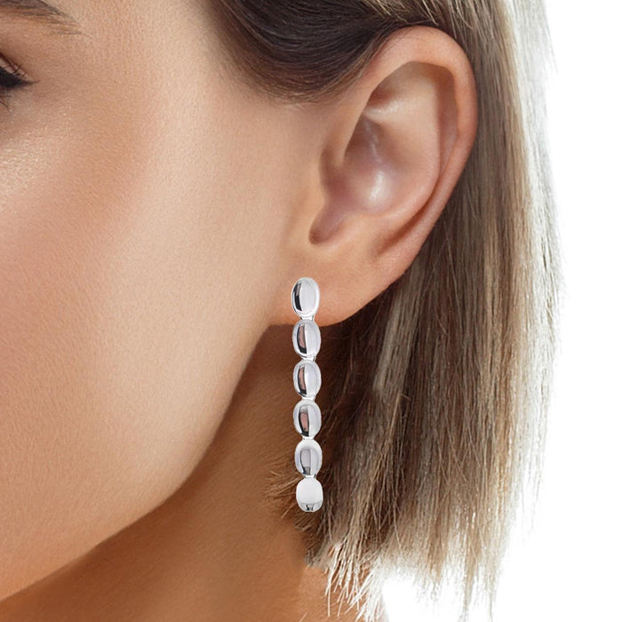 photo of blonde model wearing one  silver long six oval disk earring on a white background