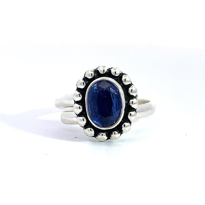 photo of a silver ring set with an oval blue gem finished with a beaded halo on a white background