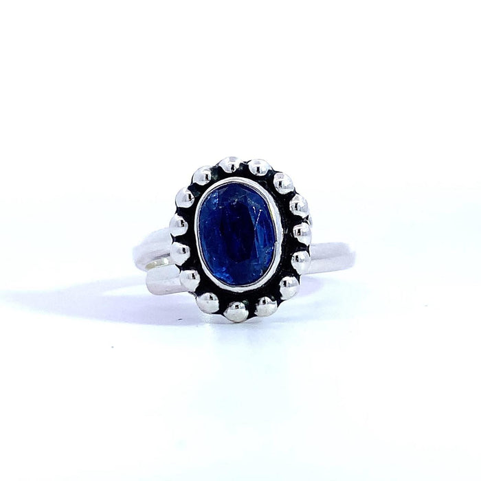photo of a silver ring set with an oval blue gem finished with a beaded halo on a white background