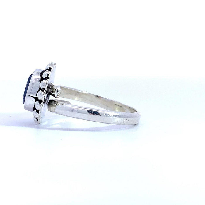 photo of a silver ring set with an oval blue gem finished with a beaded halo on a white background side view