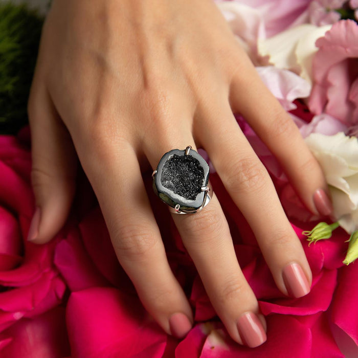 photo of a models hand wearing a black geode silver ring on a bed of flower petals