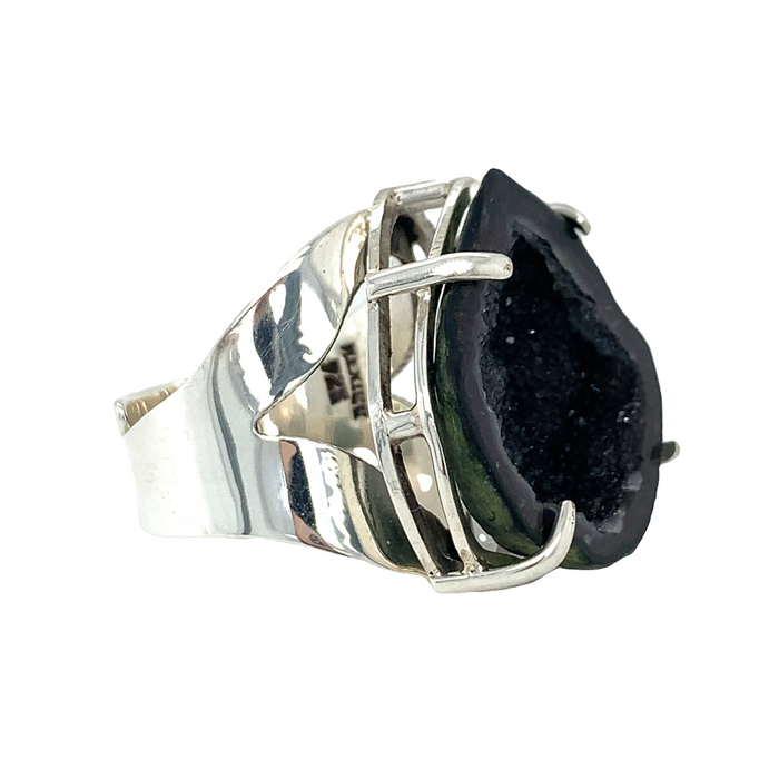 A sterling silver ring with a black geode stone set in a silver head, with a bypass shank at the back.
