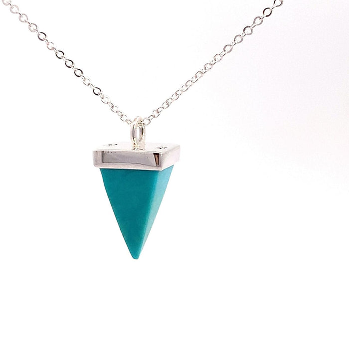 photo of a silver pendant set with a pyramid-shaped blue turquoise gem on a chain on a white background