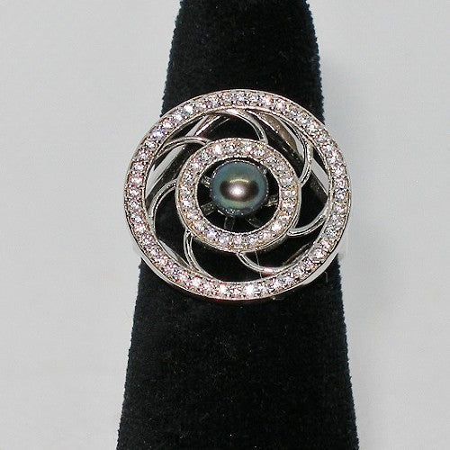 Silver ring with a central pearl and diamond-like stones on a black stand against a gray background