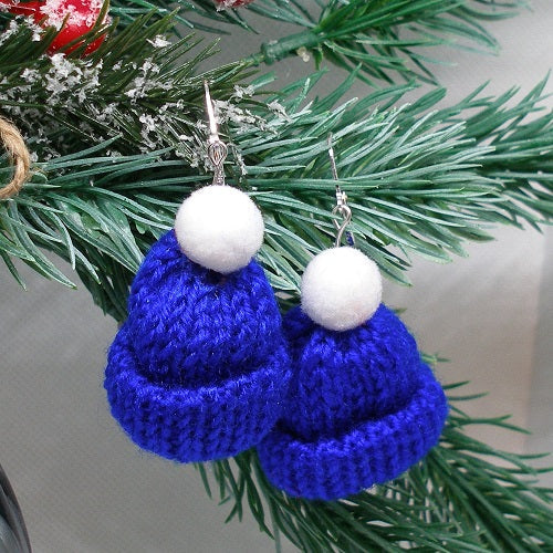 Blue knitted earrings with white pom-poms on a Christmas tree branch.