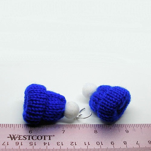 Blue knit ski hats with a white puff on top on a light gray background. Shown with a ruler to show earring size