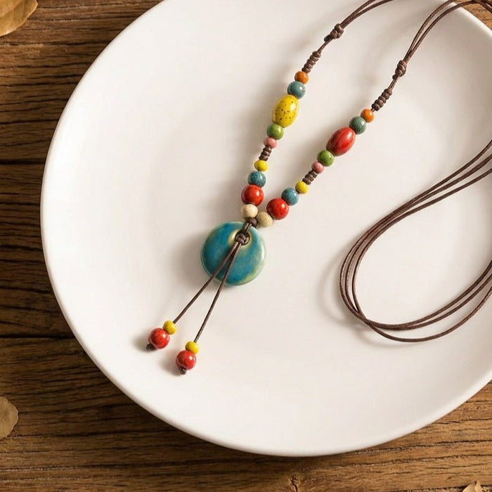 A playful mix of earthy charm and bright blue artistry, this necklace features a round turquoise-style pendant paired with colorful ceramic-style beads on a natural cord. Its free-spirited design feels cheerful, handmade, and effortlessly bohemian.