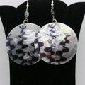 Round earrings with black and white pattern on a black stand.
