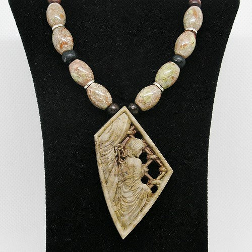 Necklace with beads and a decorative pendant on a black stand.