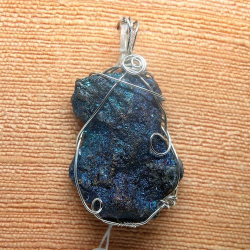 Blue stone pendant with silver wire wrapping on a textured surface