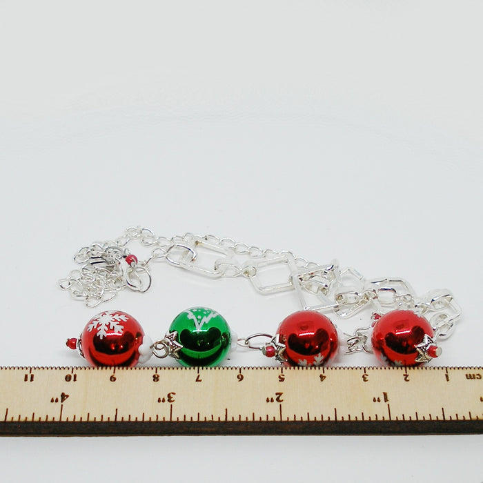 Necklace with red and green ornament charms on a white background with a ruler for scale.