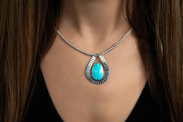 photo of a brunette model wearing a silver bead necklace with a turquoise pendant