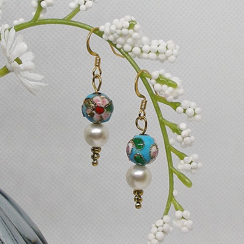 Pair of earrings with floral and pearl design hanging on a branch with white flowers.