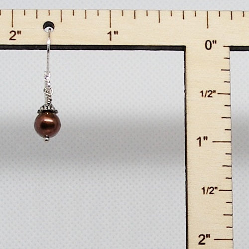 Earring with a brown bead and silver hook on a ruler for scale