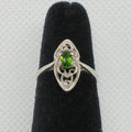 Silver ring with a green gemstone on a black velvet stand against a gray background
