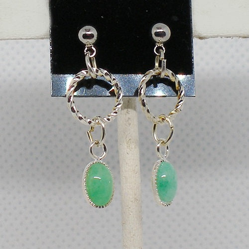 Silver earrings with green stones on a display stand.