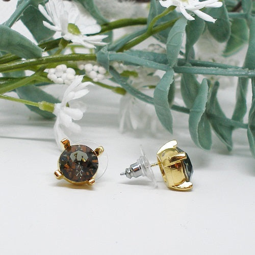 Pair of earrings with brown crystal on a white surface with green leaves and flowers in the background