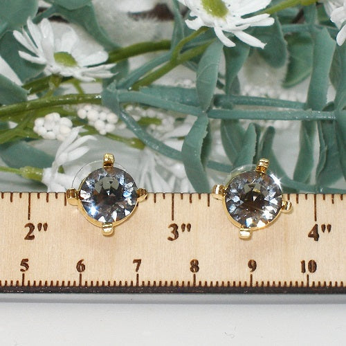 Gold earrings with dark crystals on a ruler against a floral background