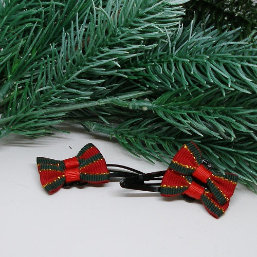 Red and green striped hair bows on black clips with a Christmas tree branch in the background