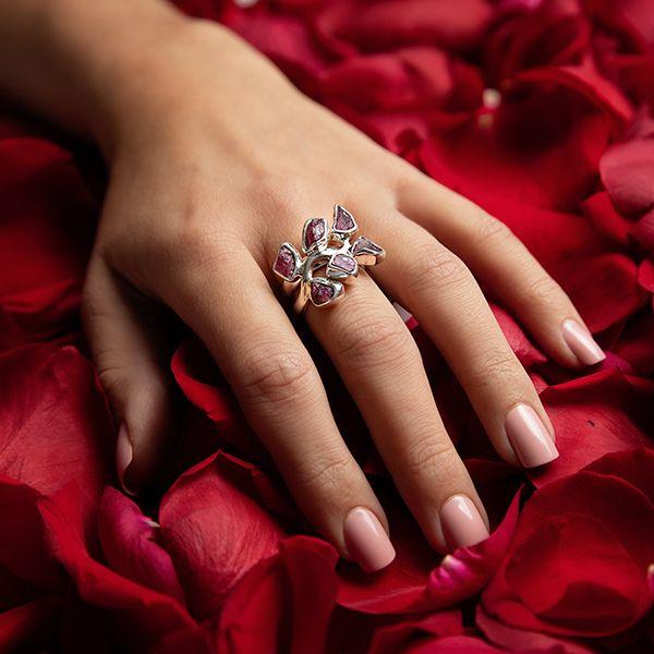 photo of a models hand wearing a silver six stone garnet ring on a bed of rose petals