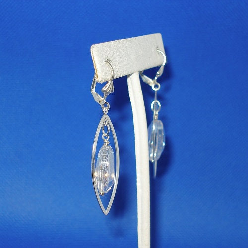 Silver earrings with clear crystals on a white stand against a blue background
