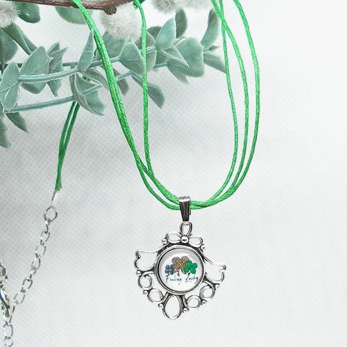 Necklace with a pendant featuring a shamrock design and text, against a light background with green leaves.