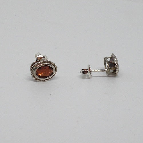 Pair of silver stud earrings with a central red gemstone on a white background