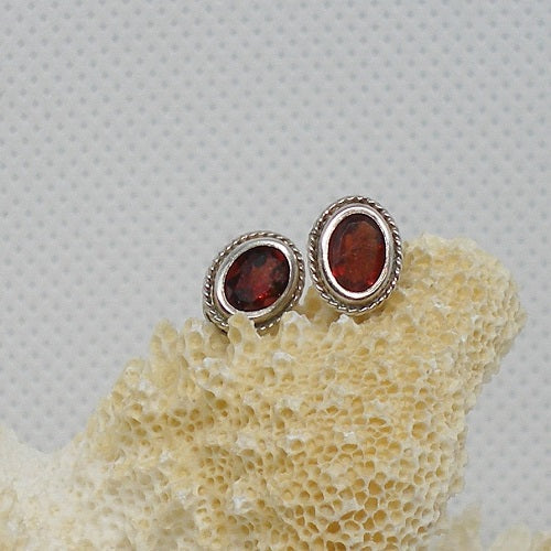 Pair of silver earrings with red gemstones on a textured beige surface