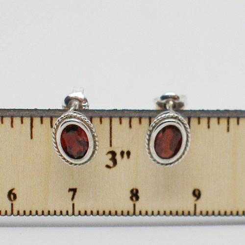 Pair of earrings with red stones on a ruler for scale