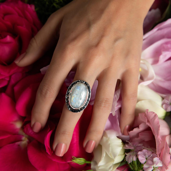 Photo of a model wearing a silver oval white moonstone ring resting on a bed of flower petals