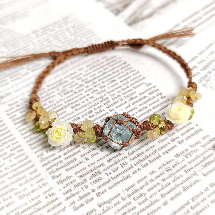 The BohoBud Bracelet brings the softest parts of nature to your wrist. Featuring a glacier-blue synthetic crystal as the centerpiece, wrapped in rustic brown thread, this bracelet is adorned with tiny gemstone chips and mini white rose buds that look freshly picked from a meadow. Each knot is intentional, each detail handwoven, making it feel like a warm afternoon hug.