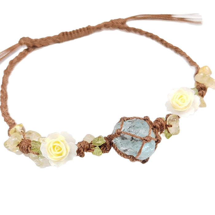 The BohoBud Bracelet brings the softest parts of nature to your wrist. Featuring a glacier-blue synthetic crystal as the centerpiece, wrapped in rustic brown thread, this bracelet is adorned with tiny gemstone chips and mini white rose buds that look freshly picked from a meadow. Each knot is intentional, each detail handwoven, making it feel like a warm afternoon hug.