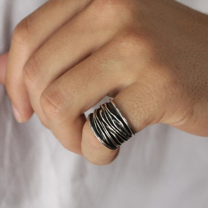 male model wearing A sterling silver wide band ring with organic texture and a dark oxidized finish