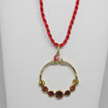 Gold hoop pendant with red and yellow stones on a red cord against a white background