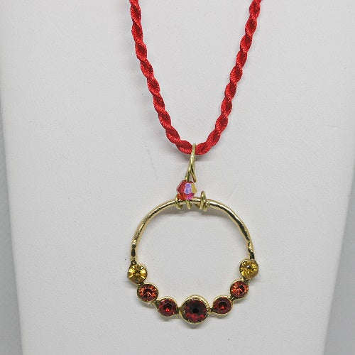 Gold hoop pendant with red and yellow stones on a red cord against a white background