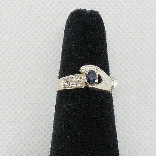 Silver ring with a blue gemstone on a black velvet stand against a light gray background