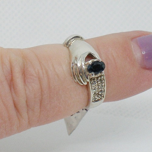 Silver ring with a black gemstone on a finger against a white background