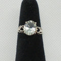 Silver ring with a large gemstone on a black stand against a gray background