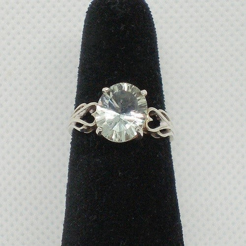 Silver ring with a large gemstone on a black stand against a gray background