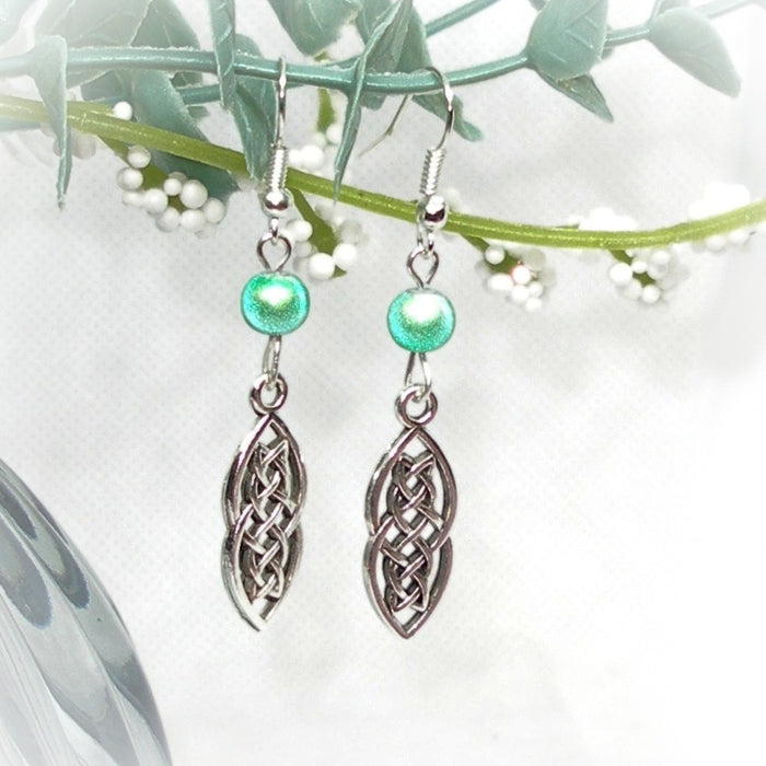 Pair of silver earrings with green beads on a white background with green leaves.