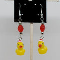 Earrings with yellow rubber duck charms and red beads on a card against a white background