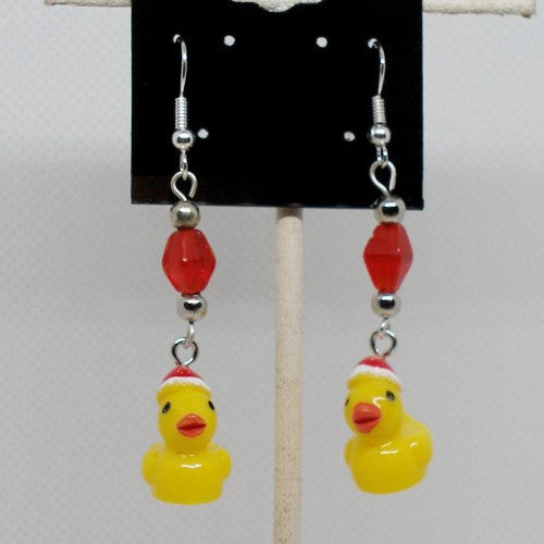 Earrings with yellow rubber duck charms and red beads on a card against a white background